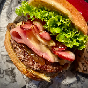 Pão brioche,  maionese,  carne artesanal blend 150g,  queijo mussarela,  presunto,  bacon fatiado,  ovo,  cebola caramelizada,  alface,  tomate. Acompanha fritas.